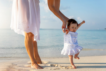 Mutter in weißem Sommerkleid hält ihre kleine Baby Tochter am Strand um laufen zu lernen