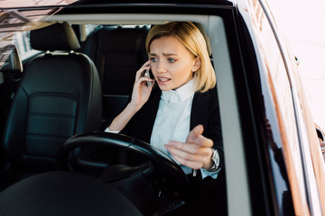 Fototapeta na wymiar upset blonde woman talking on smartphone while gesturing in car