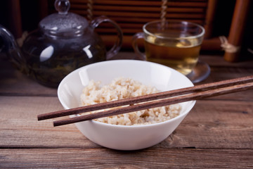 Cooked brown rice in white bowl with chopsticks on the wooden background.