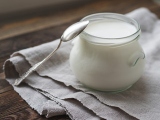 Natural homemade yogurt in a glass jar. Healthy food for breakfast. Linen tablecloth and silver spoon on on wooden table.