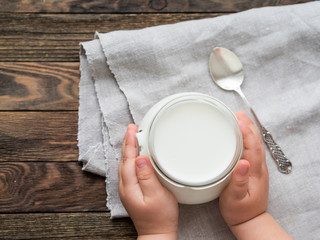 Natural homemade yogurt in a glass jar. Healthy food for breakfast in child's hands. Kid holding jar with sour cream on linen tablecloth on on wooden table.
