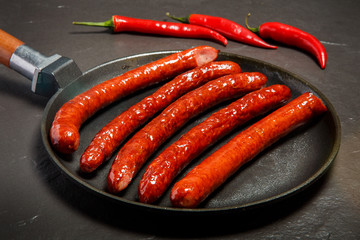 big round black pan with five long fried hunting sausages