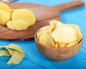Potato chips and potato on wooden backround.