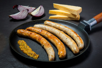 closeup black pan with fried thin sausages and granular mustard