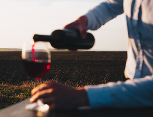 A person who serves red wine at sunset