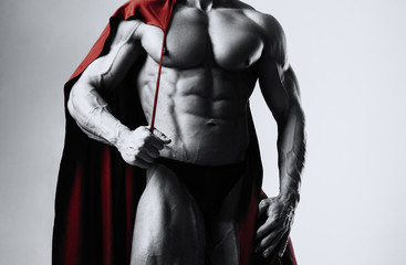 Fototapeta na wymiar Male bodybuilder puts on his shoulders a red cloak with a serious face