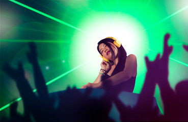 young attractive and happy Asian Japanese DJ woman remixing using deejay gear and headphones at night club with lights background in clubbing music concept