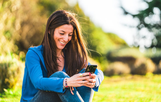 portrait of young woman using smartphone sitting on grass in park