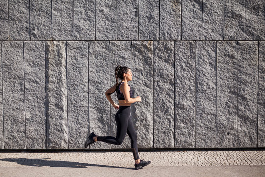 beautiful and brunette woman running on a sunny morning with a granite wall in the background