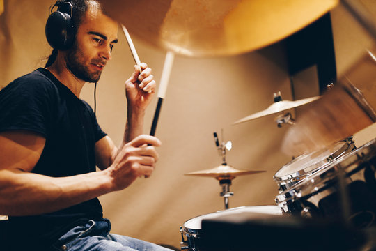 Positive handsome male with headphones playing on drums in studio