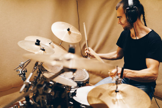 Positive handsome male with headphones playing on drums in studio