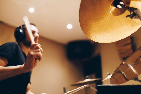 Positive handsome male with headphones playing on drums in studio