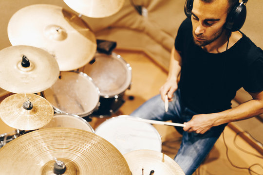 Positive handsome male with headphones playing on drums in studio