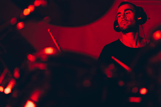 Male holding drumsticks and playing on drums in redness