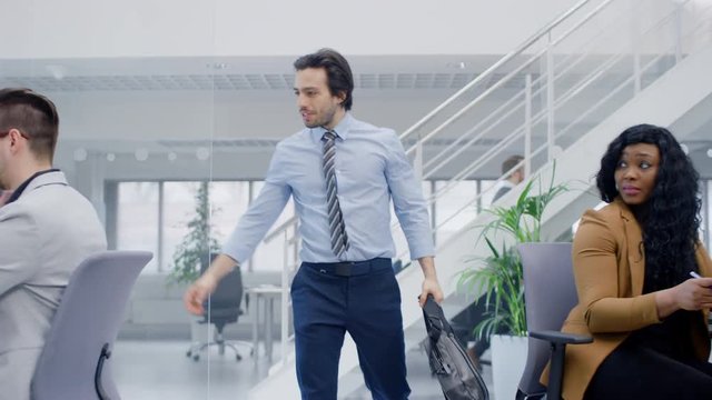 Young Happy Businessman Returns to Work After Vacation, Walks Into Bright Modern Office, Greets Everybody, Takes Place at His Desktop Computer. 