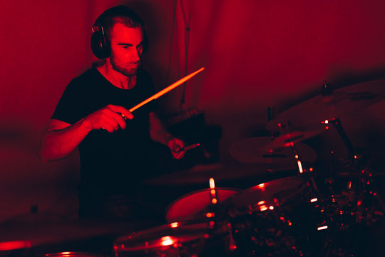 Male holding drumsticks and playing on drums in redness