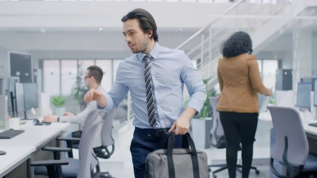 Young Happy Businessman Returns to Work After Vacation, Walks Into Bright Modern Office, Greets Everybody, Takes Place at His Desktop Computer. 