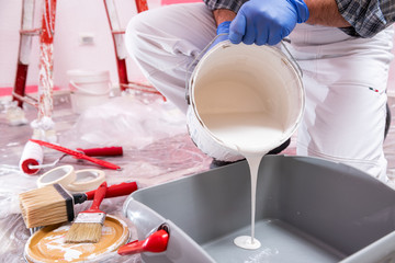 Caucasian house painter worker in white overalls, pour the white paint into the container. Construction industry. Work safety.