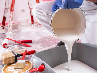 Caucasian house painter worker in white overalls, pour the white paint into the container. Construction industry. Work safety.