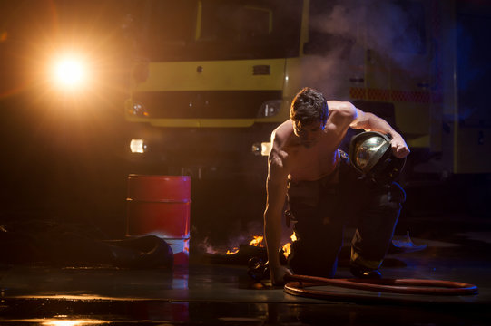 Shirtless muscular male in fireman uniform sitting on burning floor during dangerous mission