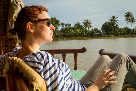 Side view of attractive young woman looking away while resting on comfortable lounger on terrace near calm sea in India