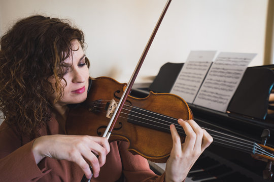 Woman sitting next to a piano playing a violin
