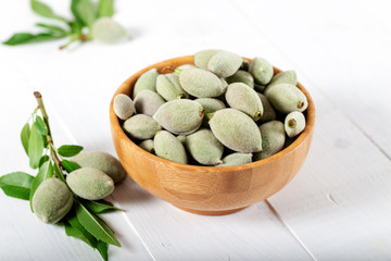 Fresh green almonds in wooden bowl on white background.