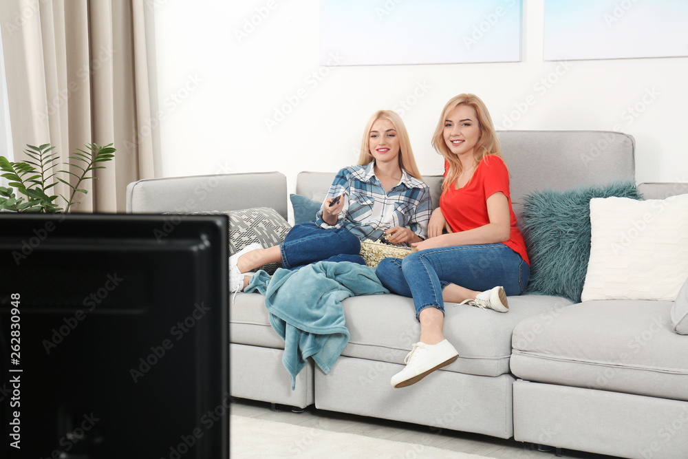 Sticker Young women with bowl of popcorn watching TV on sofa at home