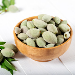 Fresh green almonds in wooden bowl on white background.