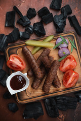 Barbecued balkan cevapcici or skinless beef sausages, flatlay on a rusty metal background with charcoals