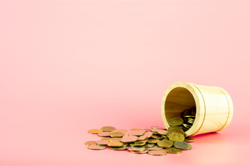 Stack of gold coins from the wooden basket on pink background.