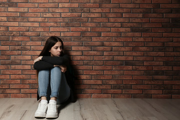 Upset teenage girl sitting on floor near wall. Space for text