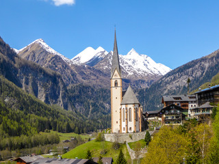 Little church in Heiligenblut, Austria, located in the valley, between Alpine mountains. Lots of trees. Beautiful for holidays. Grossglockner group in the back