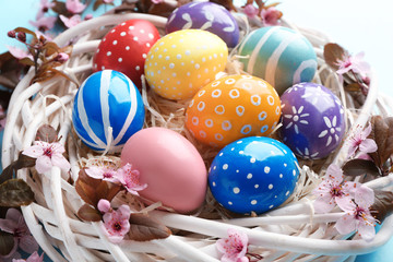 Fototapeta na wymiar Painted Easter eggs in nest with flowers on color background, closeup