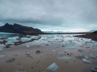 Thousands of smaller icebergs in different shades of blue drifting towards the sea. The water of...