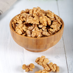 Walnut kernels in a wooden bowl on white background.