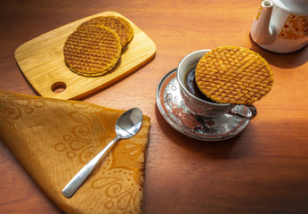 Cup of coffee covered with a stroopwafel and a group of stroopwafels