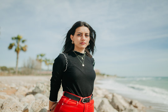 woman looking at camera in calm sea while standing on sunny day