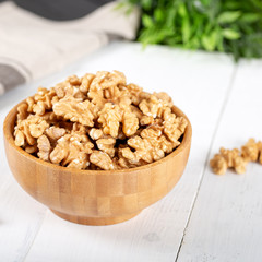 Walnut kernels in a wooden bowl on white background.