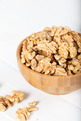 Walnut kernels in a wooden bowl on white background.