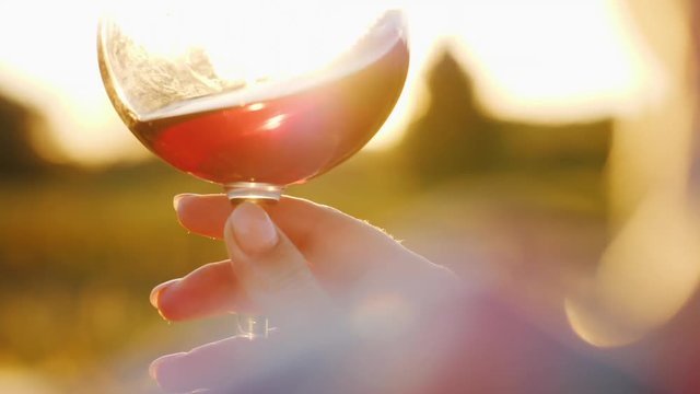 The winemaker holds a glass of red wine, looks at him in the sun. Close-up. Slow motion video