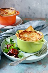 Potato gratin baked in filo dough, with crispy cheese crust and with a salad of arugula, sun-dried tomatoes and cheese on a blue background. A dish of french cuisine