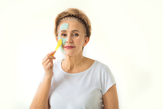 stylish beautiful elderly woman with a short haircut on a white background puts on a cleansing cream face mask