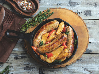 grilled chicken sausages with fried potatoes and peppers in an iron pan