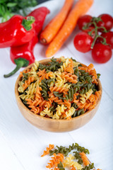 Colorful raw rotini pasta with vegetables on white background