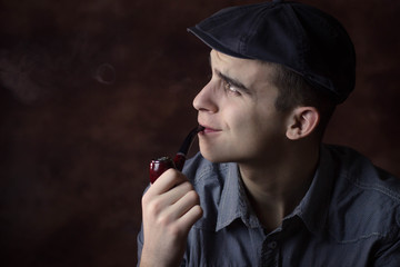 Closeup portrait of young man with beret hat, smoking a tobacco pipe. Thinking about something. Human facial expression, emotion, feeling, sign symbol body language