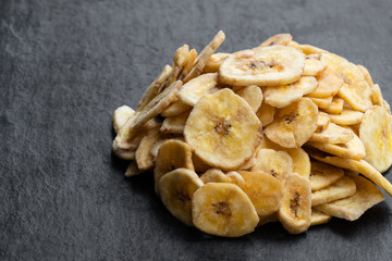 Homemade dehydrated banana chips on black stone background