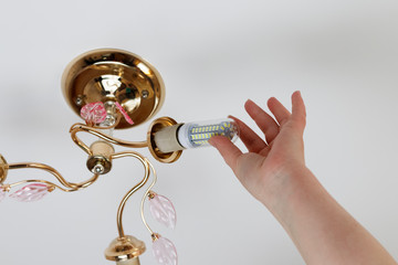 female hand inserts a light bulb into the threaded socket. Installation of household LED lamps of corn type, in the lamp holder, there is a toning