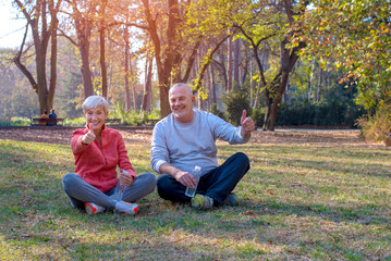 Fototapeta premium Active senior couple with thumbs up sitting on the ground and having little break after training outdoor