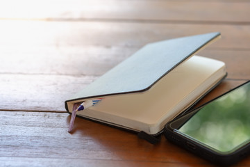 Business, education, planning and technology concept. Close up of notebook, pen with smart mobile phone on wooden table.